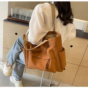 Brown canvas tote bag with side pockets shown from the back on a model in a minimal room