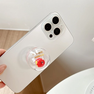 Close-up of clear phone grip with miniature red apple and golden cutlery inside