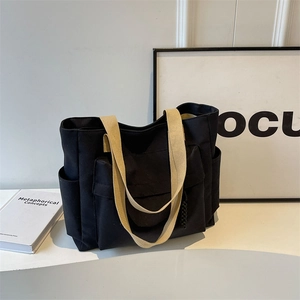 Minimalist black canvas tote bag with front pocket and beige strap for daily commute