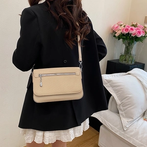 Elegant beige crossbody bag with woven texture and silver zipper detail worn by model