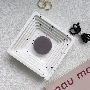 Detail view of a square tiered jewelry tray with black splattered ink pattern and round slot
