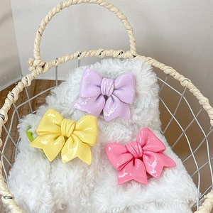 Three glossy bow-shaped hair clips in purple yellow and pink inside a wicker basket