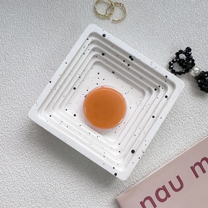 Top view of a square terrazzo tray with black ink splatters and a centered orange round piece