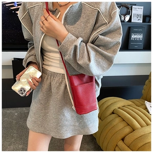 Detail of red lychee textured leather mini crossbody bag with gray sporty outfit ensemble