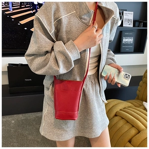 Detail of red litchi texture mini crossbody bag with matching shoulder strap on grey outfit