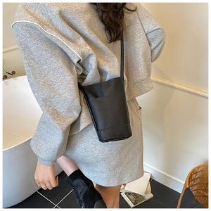 Detail of minimalist black pebbled leather bucket bag worn by model in a daily scene