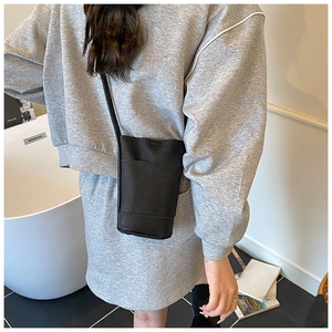 Close-up of minimalist black lychee grain leather crossbody phone bag on a person