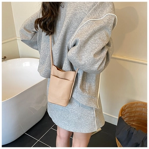 Close-up of minimalist beige lychee grain leather crossbody bag styled on a model