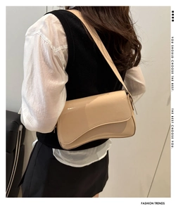 Detail view of beige baguette shoulder bag with irregular curved flap on model back