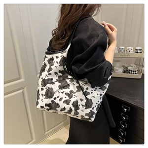 Detail of cow print tote bag showing texture and black shoulder straps on model