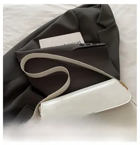 Glossy white minimalist crossbody bag detail with metallic cherry pendant on grey blazer