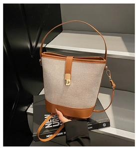 Detail of beige woven canvas bucket bag with brown PU leather trim and gold metal lock