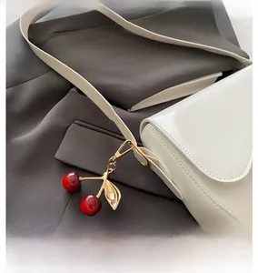Detail of red cherry charm with gold leaf hanging on a white patent leather bag
