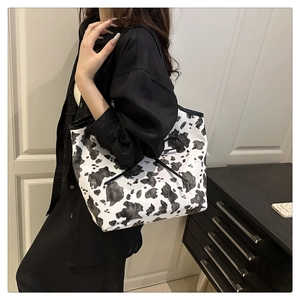 Detailed view of large cow print tote bag with black straps on shoulder of a model