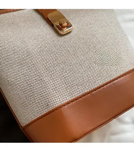 Close-up of woven canvas bucket bag with brown leather trim and golden twist lock clasp