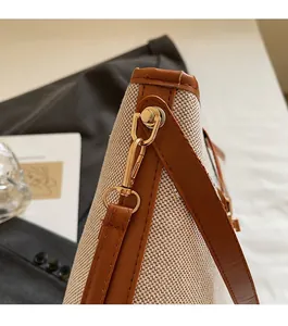 Detail of canvas bucket bag with brown leather trim and shiny gold metal lobster clasp
