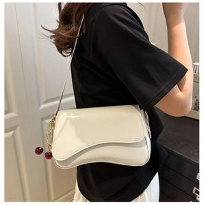 Close-up of white patent leather shoulder bag with cherry charm and wavy flap detail