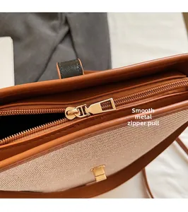 Detail of smooth metal zipper and brown leather trim on beige woven bucket bag