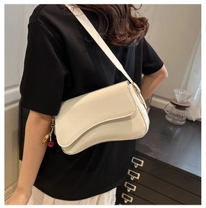 Detail view of cream white shoulder bag with unique curved flap and cherry charm