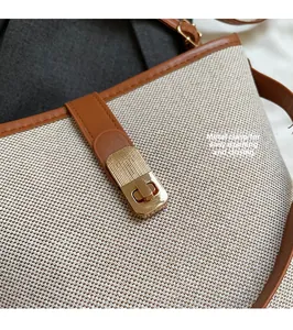 Detail view of gold hardware clasp on beige woven bucket bag with brown leather trim
