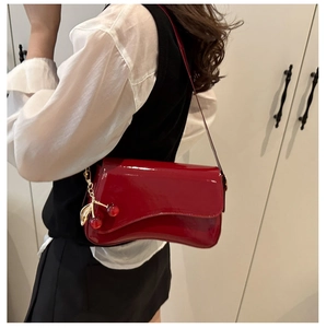 Detail of red patent leather shoulder bag with cherry pendant and wavy edge design