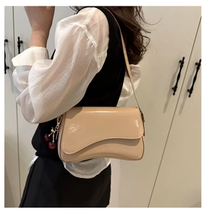 Detail of apricot patent leather shoulder bag with cherry charm and wavy flap design