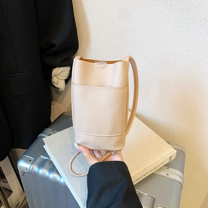 Minimalist beige pebble leather crossbody bucket bag with slender shoulder strap