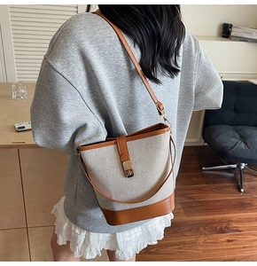 Detail of the canvas bucket bag with brown leather trim worn as a stylish shoulder bag