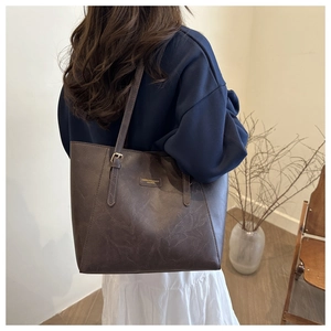 Detail of dark brown tote bag showing leather texture and gold lettering on model