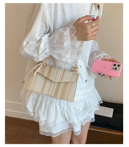 Detail of a striped straw crossbody bag worn with a white lace dress in a natural setting