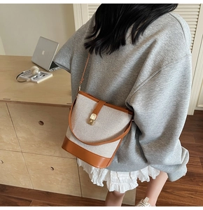 Detail of canvas bucket bag with brown leather trim and golden twist lock on a shoulder strap