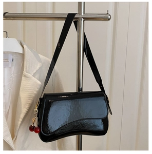 Detail of black patent leather shoulder bag with cherry charm and unique wavy base design