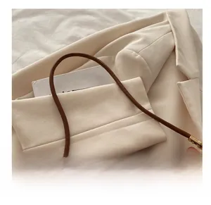 Detail of a dark brown leather handbag with slim cylindrical handles and gold hardware