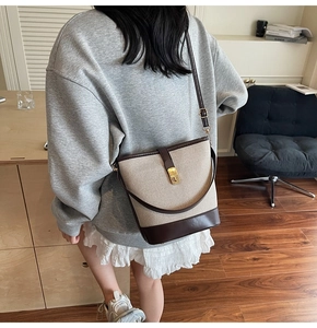 Detail of canvas bucket bag with brown leather trim and golden metal clasp closure