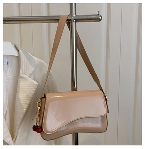 Detail of beige glossy shoulder bag with magnetic flap and a cute cherry pendant charm