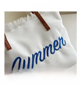 Detail of white canvas tote with Summer embroidery, fringe edges and brown leather handles