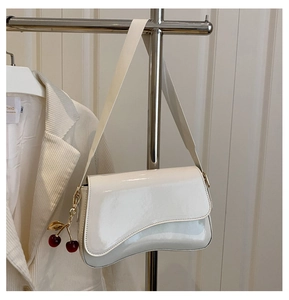 Detail of white patent leather shoulder bag with asymmetrical flap and cherry charm