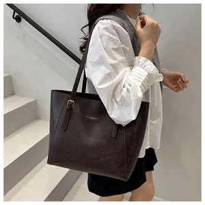 Detailed shot of dark brown tote bag featuring metallic fashion logo and adjustable strap