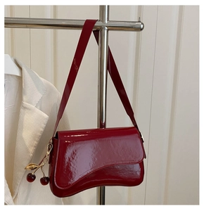Detailed view of dark red patent leather bag with glossy finish and cherry pendant charm