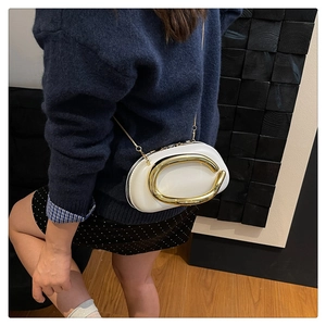 Close-up of elegant cream white crossbody bag featuring a bold golden C-shaped buckle
