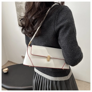 Detail view of white underarm bag with red contrast piping and golden twist lock
