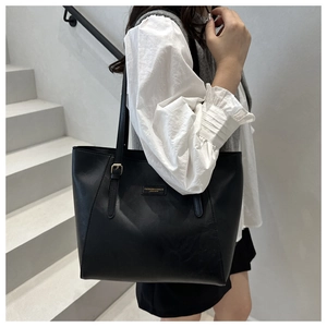 Dettaglio della borsa tote in pelle nera con logo dorato e tracolla indossata da modella