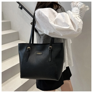 Detail of black leather tote bag with gold logo and adjustable metallic square buckles
