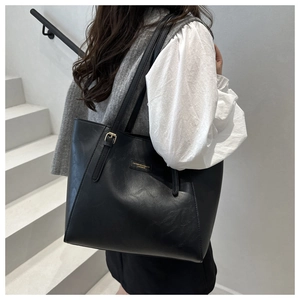 Detail of minimalist black tote bag featuring golden logo plate and side buckle accent