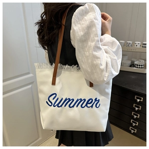 Detail of white canvas tote bag with blue Summer embroidery and brown leather shoulder strap