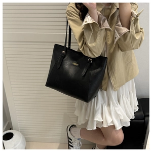 Detail of a chic black leather tote bag featuring a polished gold brand plaque on the front