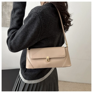 Close-up of a stylish beige baguette shoulder bag with a gold lock on a model's arm