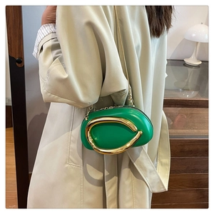 Peapod-shaped green leather crossbody bag with bold gold ring detail on model