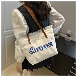 Detail of white canvas tote bag with blue Summer embroidery and brown leather straps