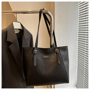 Dettaglio borsa tote in pelle nera con trama litchi e fibbia in metallo dorato lucido